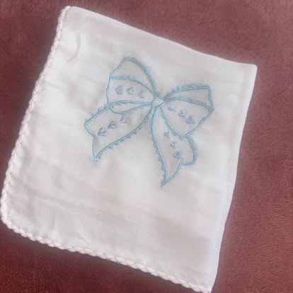 White muslin with a blue embroidered bow and scalloped edge