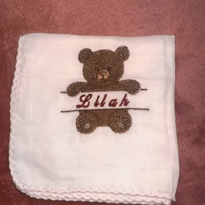 White muslin with embroidered teddy bear and the name 'Lilah'